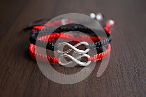Pair bracelets in black and red with infinity. Handmade woven bracelets. Handmade decorations. Background with beads with hearts