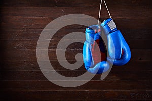 A pair of bright blue and red boxing gloves hangs against wooden background.