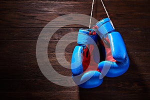 A pair of bright blue and red boxing gloves hangs against wooden background.