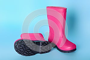 Pair of bright pink rubber boots on light blue background