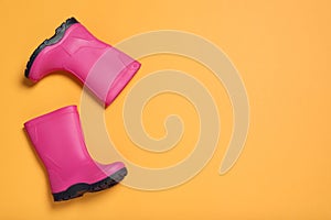 Pair of bright pink rubber boots on orange background, top view. Space for text