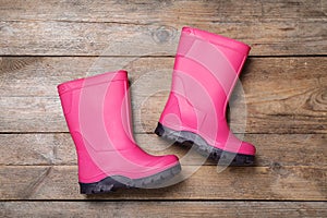 Pair of bright pink rubber boots on wooden background, top view