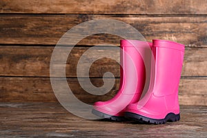 Pair of bright pink rubber boots on wooden surface. Space for text