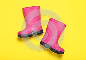 Pair of bright pink rubber boots on yellow background, top view