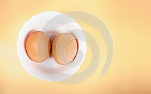 Pair of brown eggs in white bowl on pastel yellow background