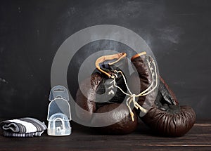 Pair of brown leather vintage boxing gloves, silicone cap and wrist bandage, wooden background