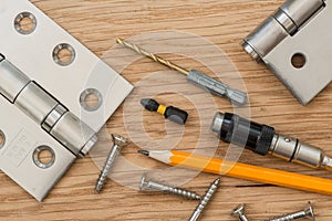 A pair of brushed steel door hinges and tools,  on wooden surface