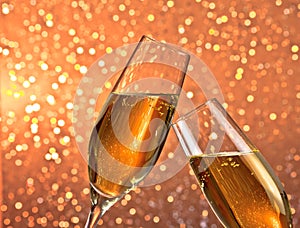 Pair of a champagne flutes with gold bubbles on light bokeh background