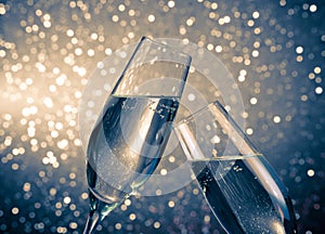 A pair of champagne flutes with golden bubbles on blue light bokeh background