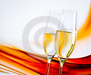 A pair of champagne flutes with golden bubbles on blur light background