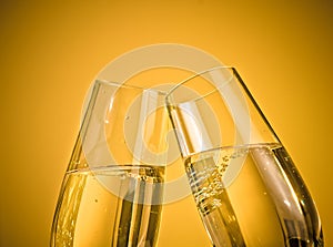 A pair of champagne flutes with golden bubbles on golden light background