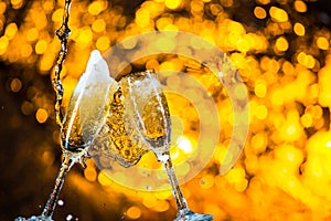 A pair of champagne flutes with golden bubbles make cheers on golden light background with space for text