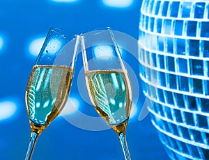 A pair of champagne flutes with golden bubbles make cheers on sparkling blue disco ball background