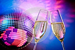 A pair of champagne flutes with golden bubbles make cheers on sparkling blue and violet disco ball background