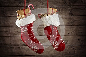 Pair of Christmas stockings filled with gifts and sweets hanging in front of a rustic wooden wall