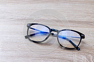 Pair of classic black reading glasses on wooden table. Glasses with filter coating blocking screen`s blue light to prevent