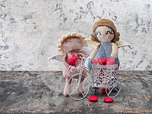 A pair of crocheted angels hold a bicycle with pink hearts, a Valentine's Day card