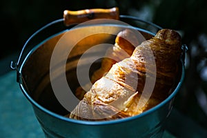 Pair of croissants in a tin bucket lit by strong morning sun li