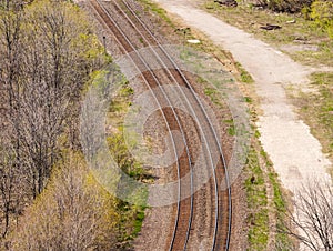 Pair of curving train tracks near forest.
