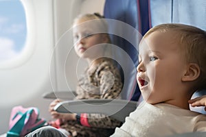Pair of cute little adorable sibling brother and sister traveling by plane. Boy and girl sit inside aircraft during flight.
