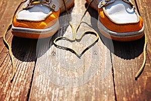 A pair of deck shoes on a nice wooden porch with the laces in a heart shape