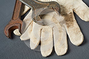 Pair of dirty textile protective gloves for repair or other hard works with old rusty metal wrench