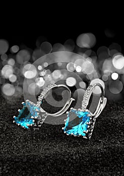 Pair of earrings with gems topaz and diamonds on black background with bokeh