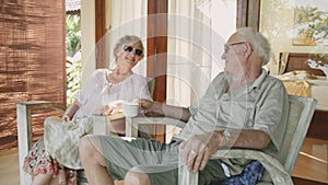 Pair of elderly people in sunglasses sitting in the front yard of their house