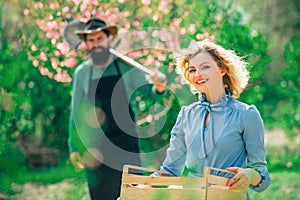 A pair of farms carries boxes with vegetables and greens along the field. Cheerful couple of farmers standing in