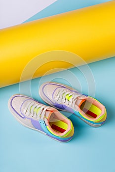 Pair of fashionable bright sports shoes for teens standing on orange-blue background.