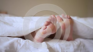 Pair of feet in bed on white sheets. Child lies in bed in the morning and moves his legs