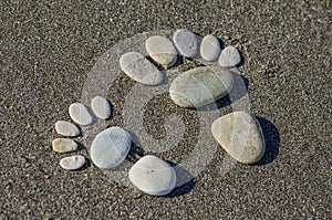 Pair of feet made of sea stones on coarse sand
