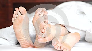 Pair of feet playing footsie under the covers at home in bed