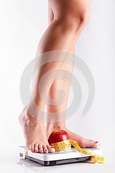 A pair of female feet standing on a bathroom scale with red apple