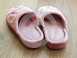 Pair of female house slippers on a brown wooden floor. Cozy, warm and comfortable pink domestic shoes