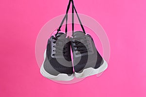 Pair female sports sneakers for run and fitness hanging by shoelaces on pink background. Fashion stylish sport shoes.