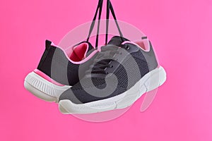 Pair female sports sneakers for run and fitness hanging by shoelaces on pink background. Fashion stylish sport shoes