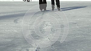 A pair of figure skaters in black skates learn a waltz on ice outdoors