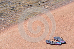 Pair of Flip Flops at Shoreline of Sandy Beach
