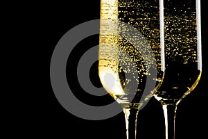 A pair of flutes of champagne with golden bubbles on black background