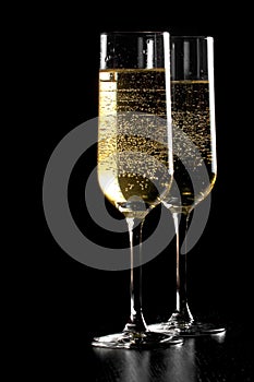 A pair of flutes of champagne with golden bubbles on black wood background
