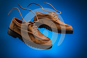 Pair of flying leather boat shoes of wheat or brown nubuck with flying laces on a blue background