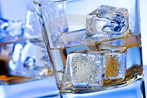 A pair of glasses of alcoholic drink with ice on disco blue light