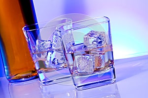 A pair of glasses of alcoholic drink with ice on disco blue light