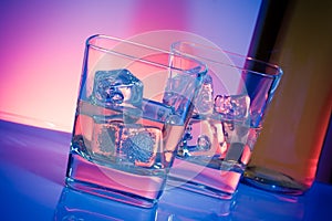 A pair of glasses of alcoholic drink with ice on disco violet light