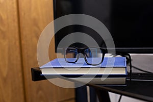 Pair of glasses on a book against a computer on the table