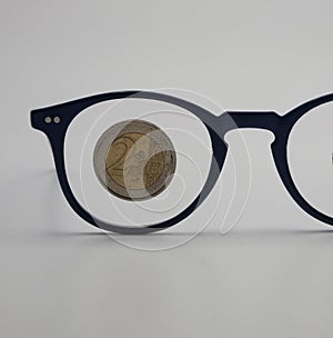 A pair of glasses with a  coin over a lens .Economic, financial concept