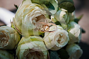 A pair of gold wedding rings on a bride's bouquet with white flowers