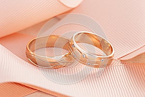 Pair of gold wedding rings with diamonds on pink ribbon background