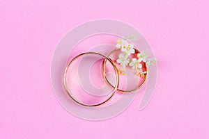 A pair of gold wedding rings and small white flowers in a ring on a pink background, top view